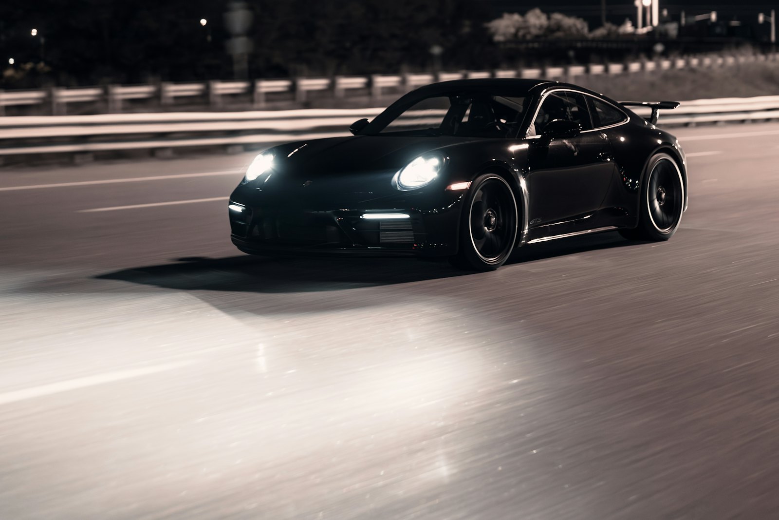A black sports car on a road at night, headlights on
